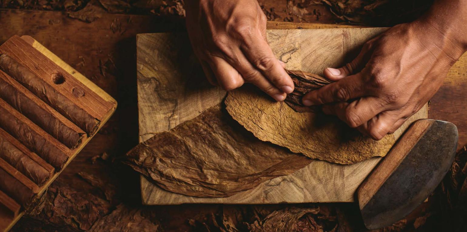A smoking cigar and a glass of whiskey on a dark wooden table