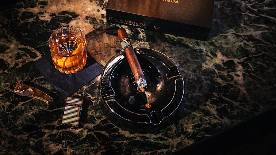 A cigar in an ashtray with an Old Fashioned on marble