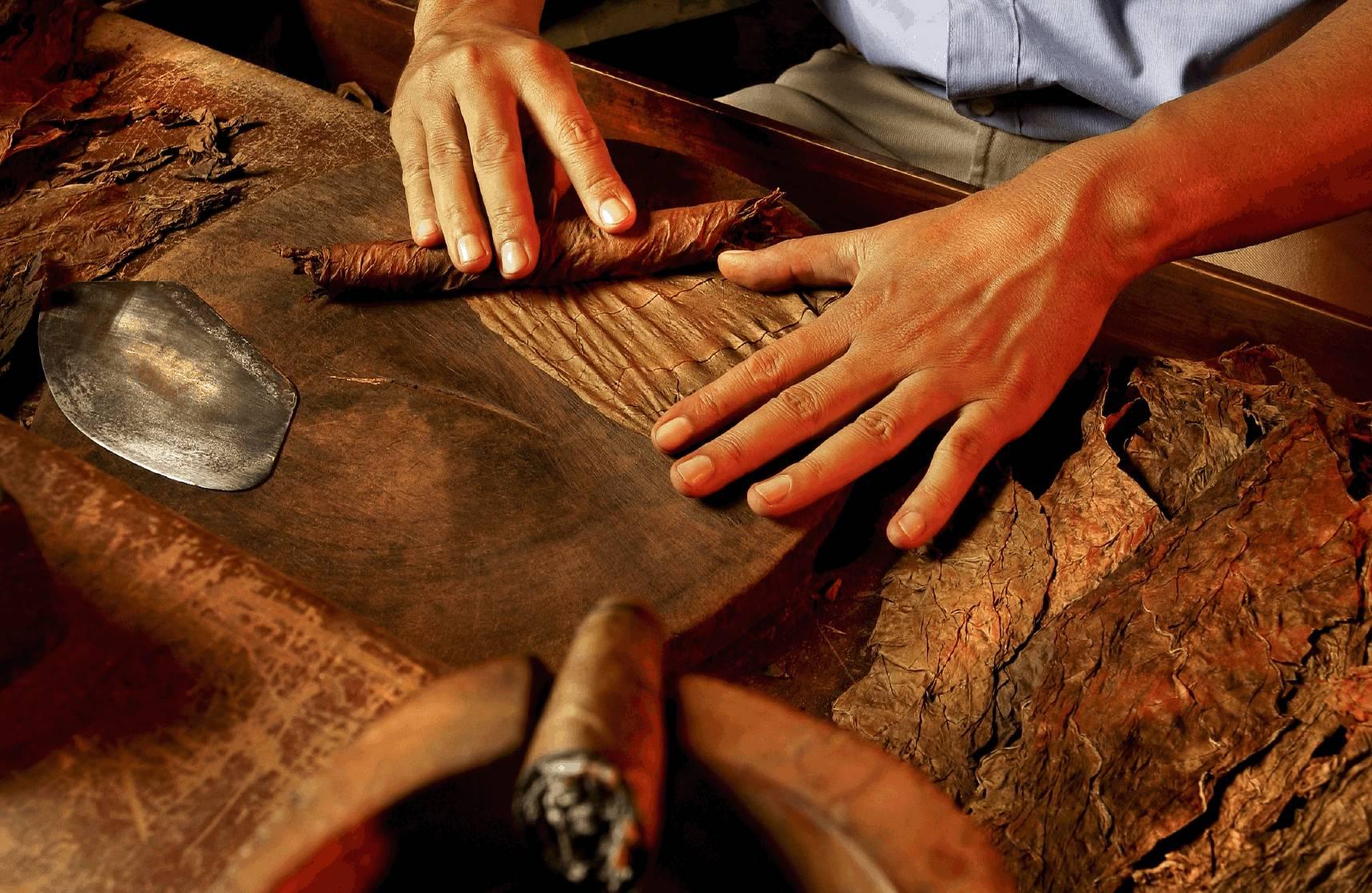 A lit cigar resting beside a glass of whiskey with rising smoke